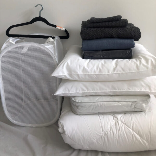 A white laundry basket and some pillows on top of the bed.